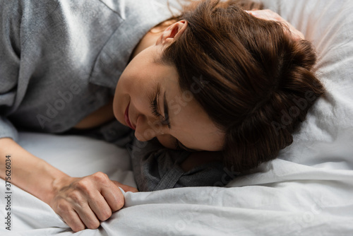 selective focus of frustrated and brunette woman touching bedding while crying on bed