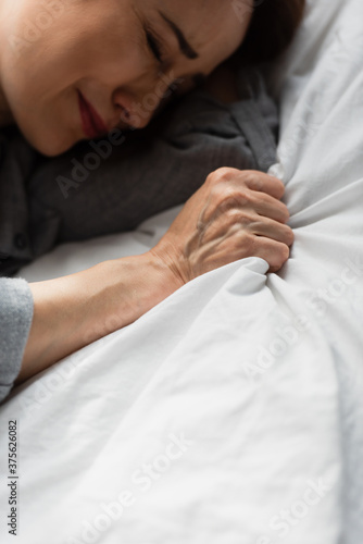 top view of frustrated and brunette woman touching bedding while crying on bed