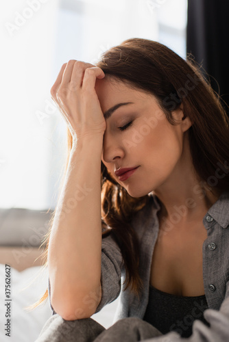 Depressed brunette woman with closed eyes touching face at home