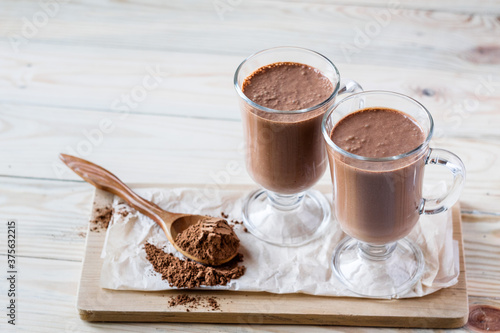 Coffee latte macchiato or hot chocolate in two glasses on wooden background, a spoon with cocoa powder. Selective focus, copyspace