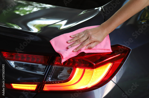 Closeup of woman owner's hand with pink   microfiber cloth cleaning at rear side of dark grey car. © Amphon