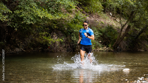 Fototapeta Naklejka Na Ścianę i Meble -  Young man in sports equipment running in mountain river 