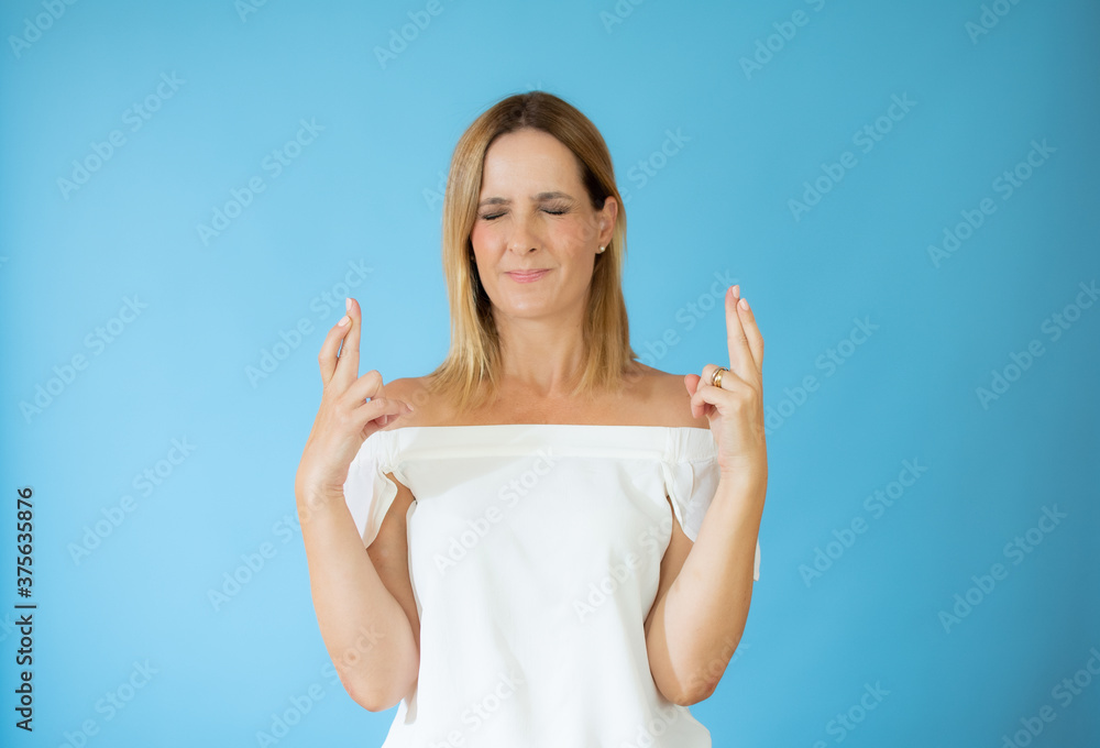 Beautiful woman in white shirt with fingers crossed gesture
