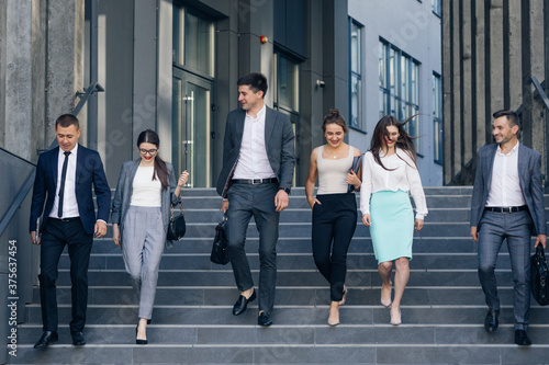 Confident team members walking on stairs. Business men and women in formal suits go and talk on the background of modern office building