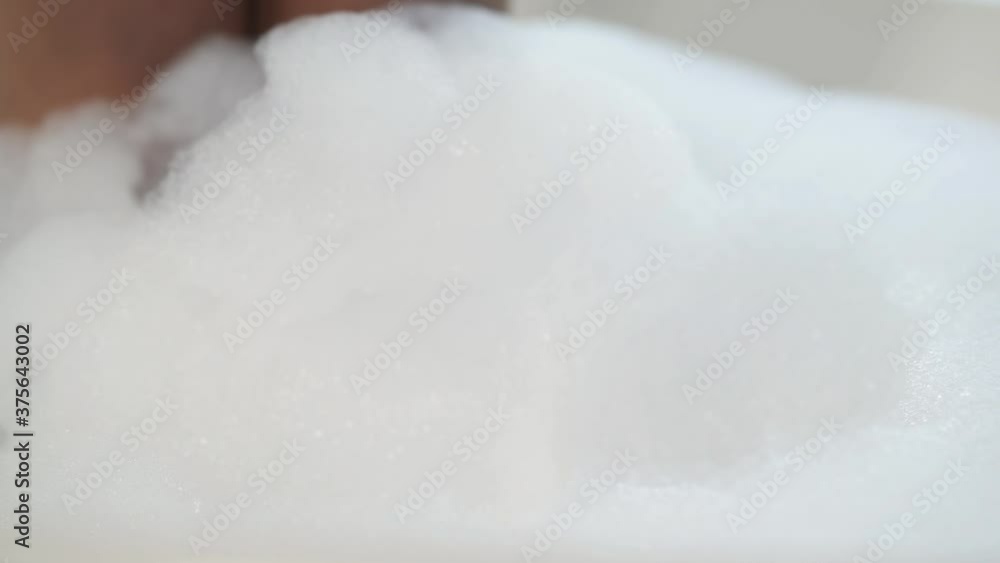 Close up of African American woman's hand in foam bath. Playing with foam bubbles in bathtub. Close up of African American woman's hand in foam bath. Playing with foam bubbles in bathtub.