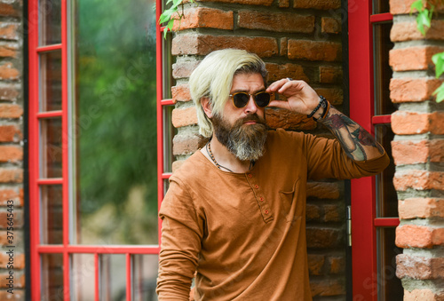 Fashion. enjoy weather this spring. male fashion style. he wear casual. brutal hipster with long beard and dyed hair. mature student relax outdoor. have a rest. thoughtful hipster at brick wall