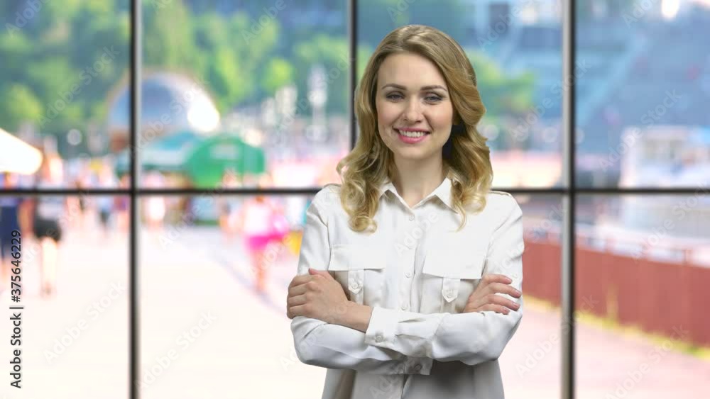 Young smiling business woman looking at camera. Happy business lady with crossed arms standing at office windows background. Young smiling business woman looking at camera. Happy business lady with crossed arms standing at office windows background.