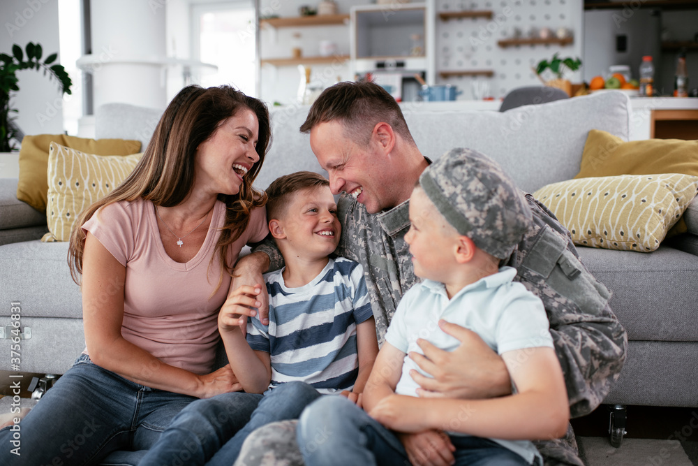 Happy soldier sitting on the floor with his family. Soldier and his wife enjoying at home with children..
