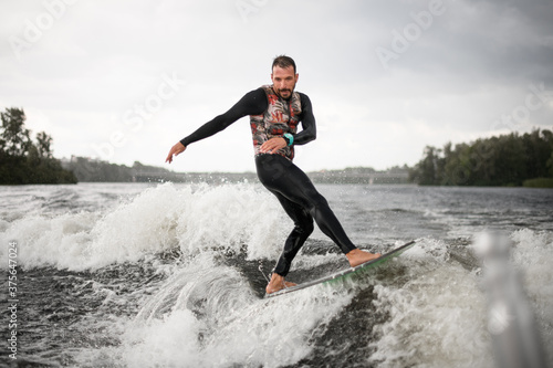 man in swimsuit surfing on surfboard trails behind boat. © fesenko