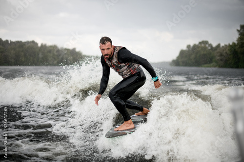adult man is surfing on surfboard trails behind boat.