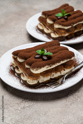 Two portions of Classic tiramisu dessert on ceramic plate on concrete background