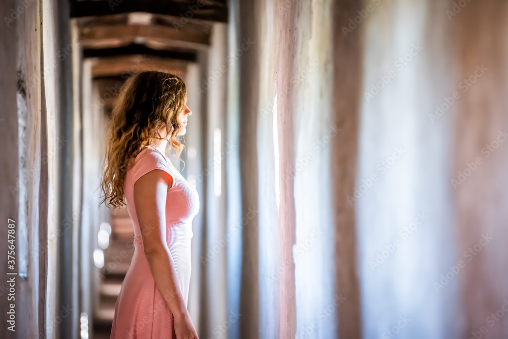 Young woman in pink dress side profile standing looking through window of wall of fortress tunnel passage in Castiglione del Lago in Italy Young woman in pink dress side profile standing looking through window of wall of fortress tunnel passage in Castiglione del Lago in Italy