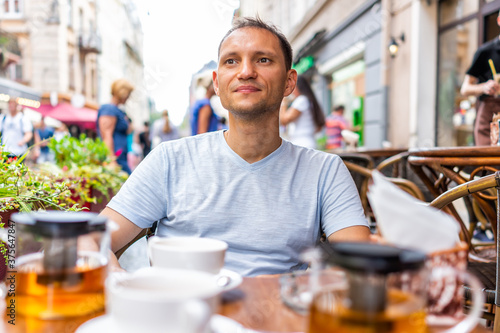 Young man sitting drinking green tea in European outdoor cafe restaurant looking at people watching in summer in Lviv or Lvov, Ukraine city at table