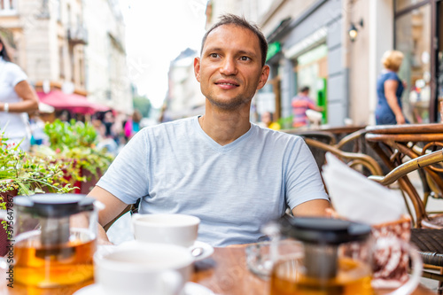 Young man happy sitting drinking green tea in European outdoor cafe restaurant looking at people watching in summer in Lviv or Lvov, Ukraine city at table