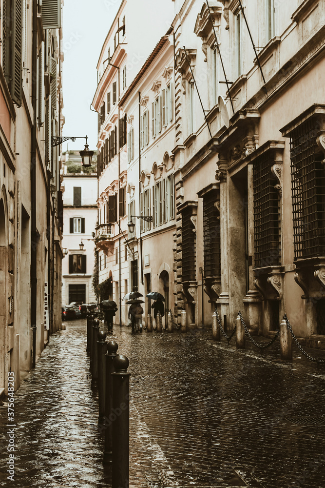Beautiful rainy street of Rome with people under umbrella silhouettes for lifestyle design. Summer season. Dark and moody background. Beautiful romantic background. Tourism concept.
