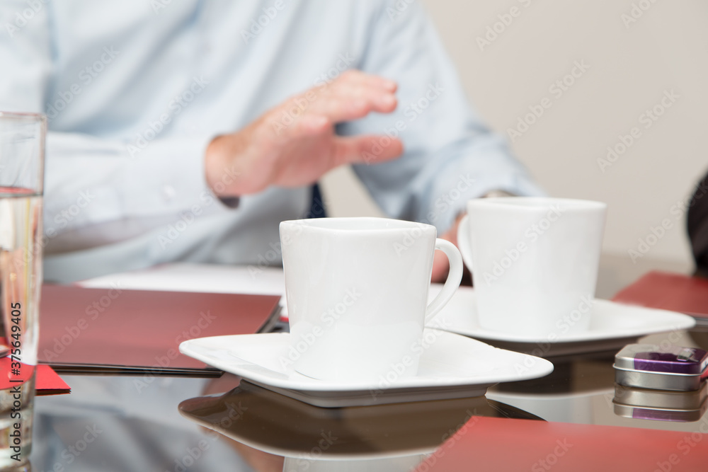 glass table with white coffee cups and plates, next to documents, in the background a person in a shirt glass table with white coffee cups and plates, next to documents, in the background a person in a shirt