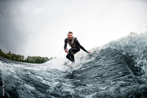 Cheerful man rides on surfboard down wave and touches the water