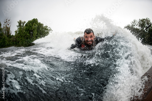 cheerful man lying on wake surfboard rides on wave from motor boat