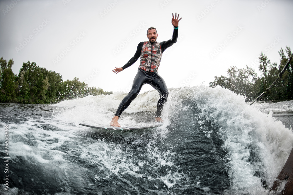 Male surfer riding foaming river wave from motorboat