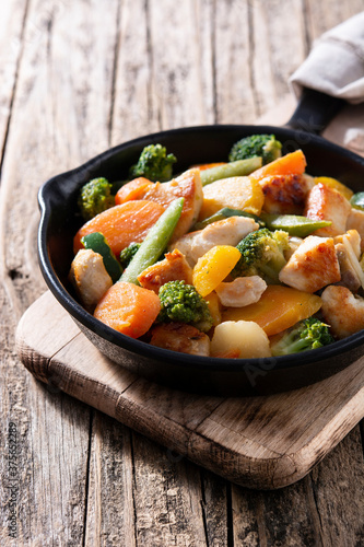 Stir fry chicken with vegetables on iron pan on wooden table