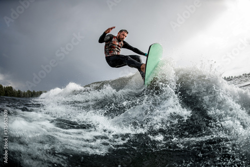 Athletic guy having fun jump on wave on surfboard in the summer day