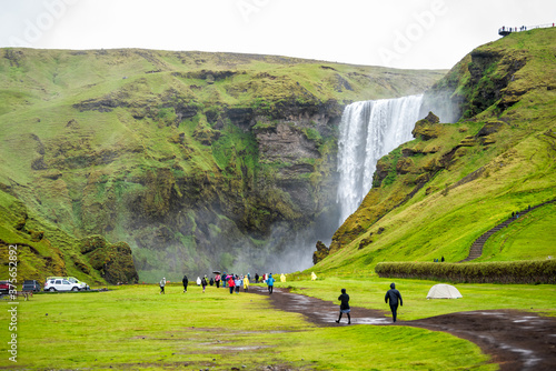 Canvas Print Skogafoss, Iceland waterfall on cliff with green grass field and many tourists p