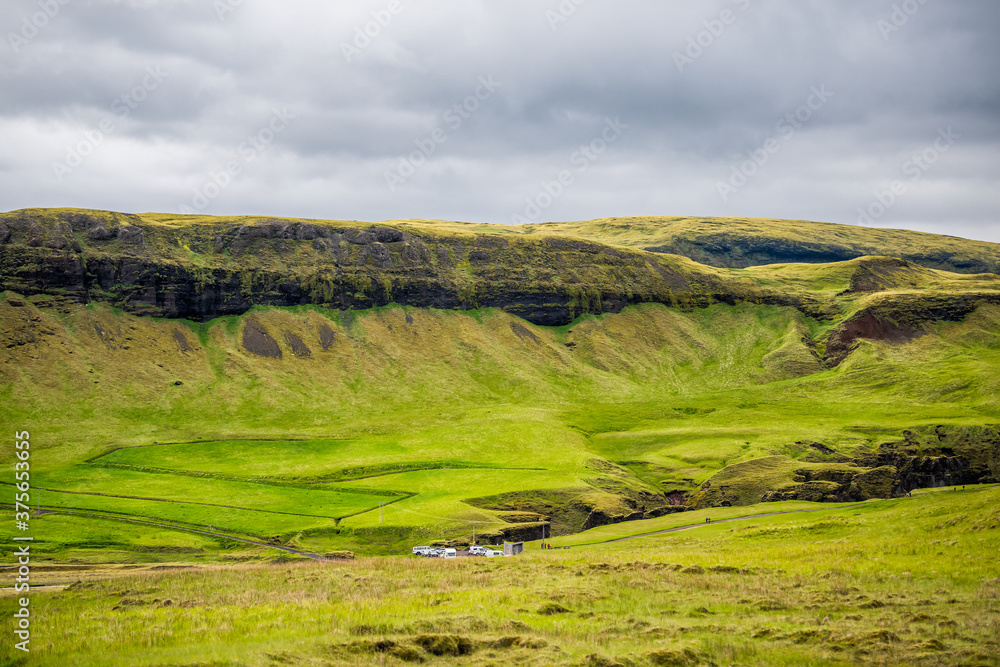 Cliff in Fjadrargljufur, Iceland with high angle view of parking lot cars by green moss grass landscape view on cloudy stormy day with clouds in sky