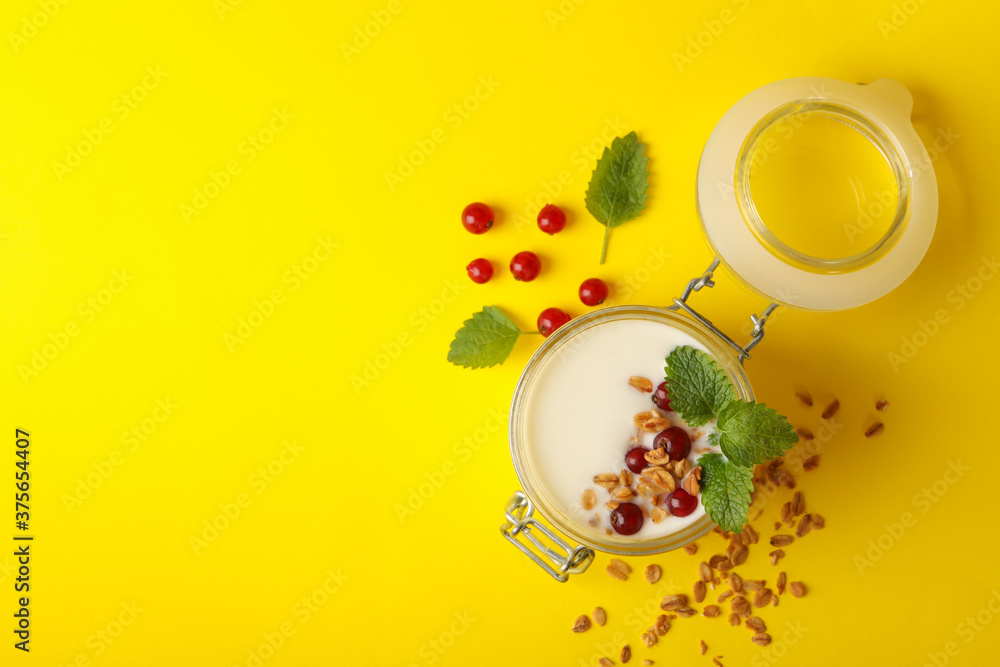 Glass jar of sour cream yogurt with cranberry, mint and granola on yellow background Glass jar of sour cream yogurt with cranberry, mint and granola on yellow background