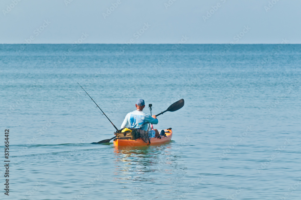  back view, far distance of a orange kayak, set up for fishing, being paddled by young, adult male, off shoreline, from a tropical beach, on gulf of Mexico, on sunny day