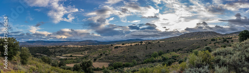 panoramic view from the mountain to the background clouds, more mountains, trees and cereal fields in the valley.