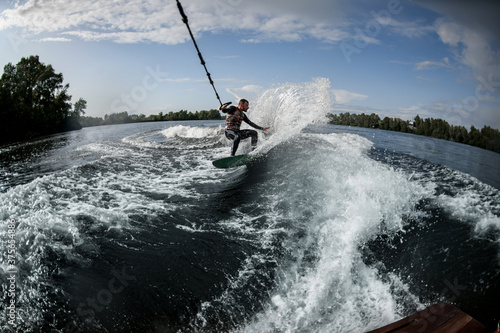 sports man holds stretched rope from motor boat and rides on wakeboard on river water © fesenko
