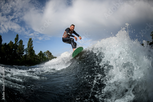 Sporty male surfer riding foaming river wave in summer sunny day