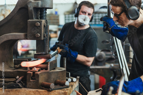 Young men working hot steel on a fly press photo