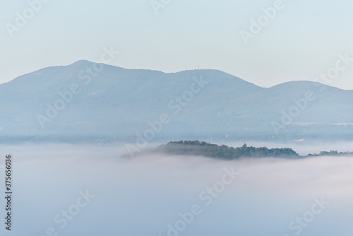 Chiusi town village mountain mist fog sunrise in Tuscany in Italy with soft clouds covering blanketing inversion in summer