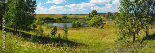 Panoramic summer rural landscape with lake and farm fields in sunny day.