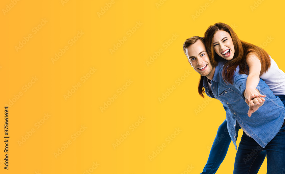 Smiling amorous funny couple. Portrait image of standing piggy back ride models in love studio concept, isolated over orange yellow background. Man and woman posing together. Copy space blank area. Smiling amorous funny couple. Portrait image of standing piggy back ride models in love studio concept, isolated over orange yellow background. Man and woman posing together. Copy space blank area.