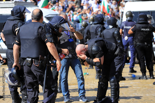 Sofia, Bulgaria on September 2, 2020: Heavily armed police officers wash their eyes from spraying tear gas, with popular non alcoholic drink