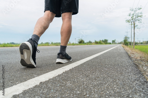The legs of male athletes in black shoes are preparing to run on the paved road Outdoor exercise for weight loss and good health.Fitness and healthy lifestyle Competition and successful concept.