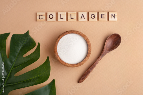 collagen powder in a wooden bowl, spoon, peach background, top view, green leaf, lettering photo