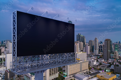 Blank black road billboard with Bangkok cityscape background at night time. Street advertising poster, mock up, 3D rendering. Side view. The concept of marketing communication to promote idea.