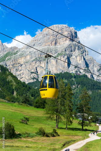 Colfosco, Val Badia - Italy: Yellow cable car connecting valley floor to high peaks of Italian Alps. Sassongher Dolomite mountain is visible in the background, surrounded by green meadows