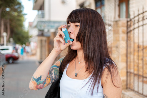 Portrait of a young woman who inhales an inhaler. There's a tattoo on my arm. Outdoor. The concept of asthma and drug dependence