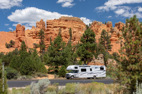 Red Canyon, UT, USA: white rv travels on a tarred road through red rock country. Pinnacles and hoodoos are visible in the background surrounded by pine trees. photo