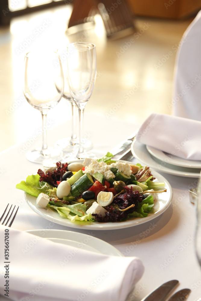 Table setting. Vegetable salad in a white plate on a light table Table setting. Vegetable salad in a white plate on a light table