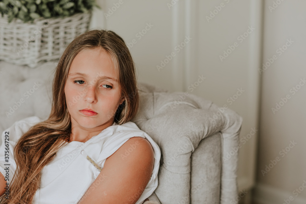 Teen girl laying on grey sofa using the thermometer looking very sad. Copy space. Teen girl laying on grey sofa using the thermometer looking very sad. Copy space.
