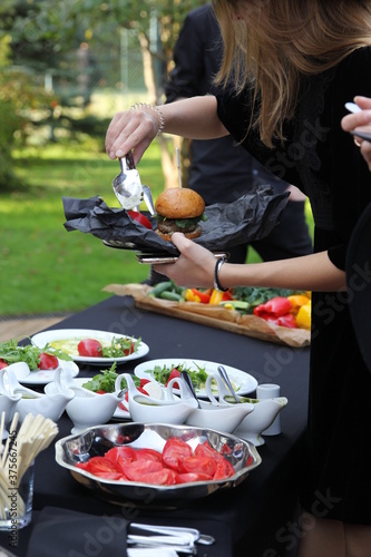 Catering. A girl in black clothes puts food on the nature. Burger  tomatoes  salads