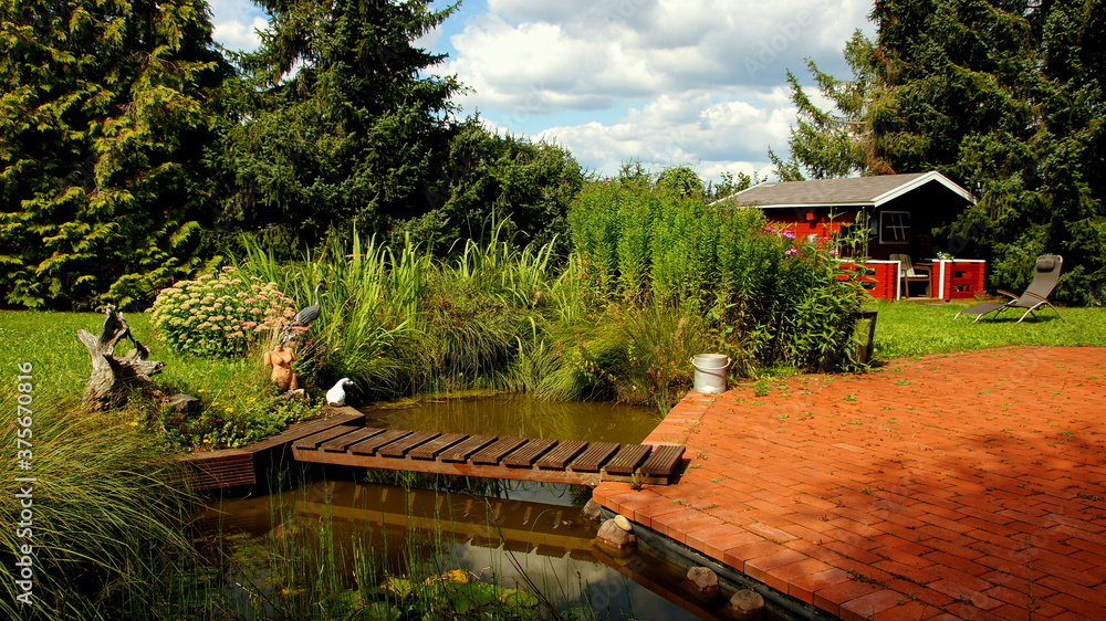 Naklejka premium romantischer Garten im Herbst mit natürlichem Teich und Holzbrücke an der Terrasse