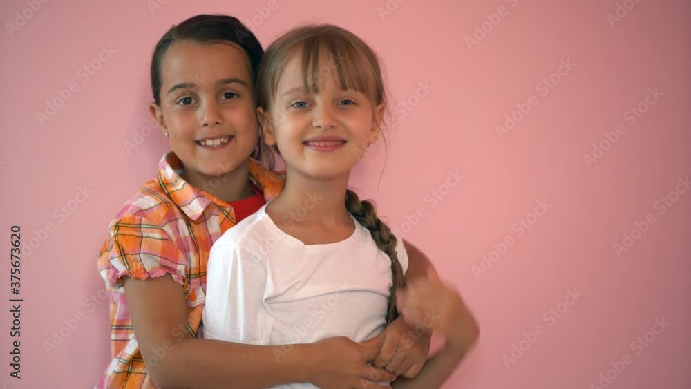 little smiling girls, sisters, best friends hug on a pink background, children hug each other little smiling girls, sisters, best friends hug on a pink background, children hug each other