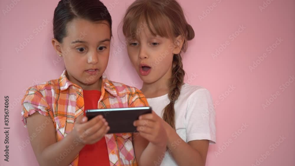 Two funny cute girls sisters learning using smartphone taking selfie at home, lenjoy social media app play game on a pink background, children and technology concept Two funny cute girls sisters learning using smartphone taking selfie at home, lenjoy social media app play game on a pink background, children and technology concept
