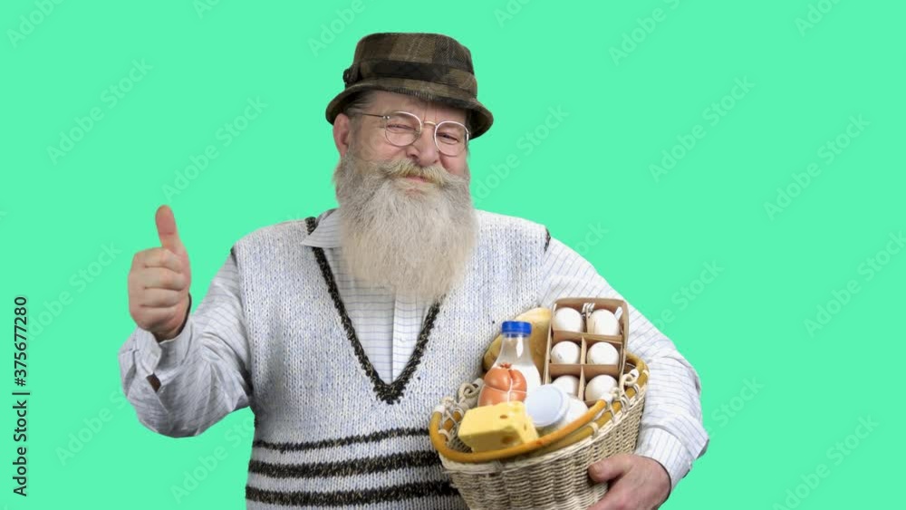 Portrait of happy farmer holding basket of dairy products. Farmer worker showing approval sign while standing with healthy food on turquoise background. Portrait of happy farmer holding basket of dairy products. Farmer worker showing approval sign while standing with healthy food on turquoise background.